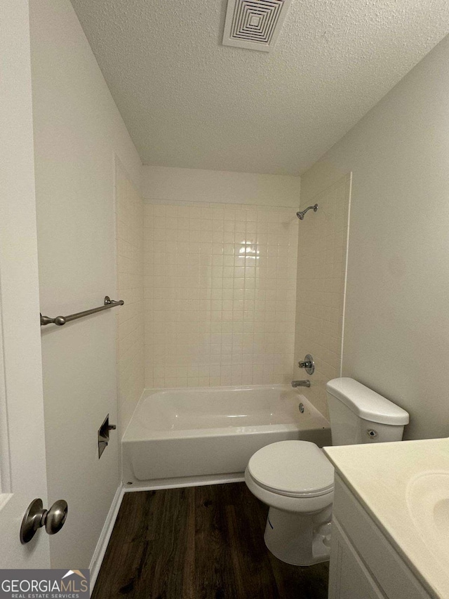 full bathroom with tiled shower / bath combo, a textured ceiling, toilet, vanity, and hardwood / wood-style flooring