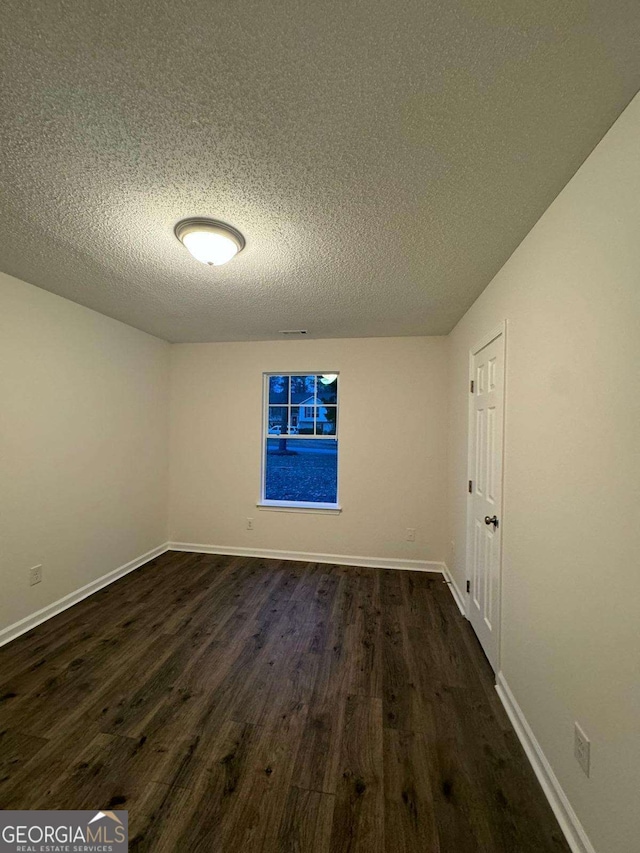 empty room featuring a textured ceiling and dark wood-type flooring