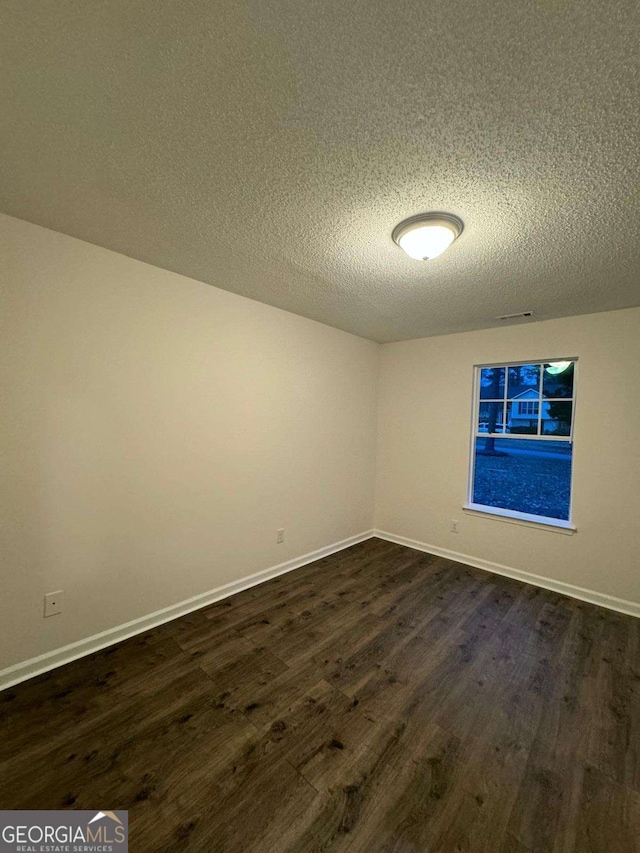 empty room with dark wood-type flooring and a textured ceiling