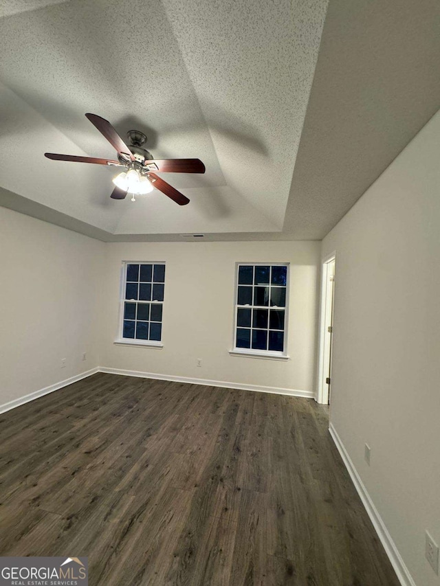 unfurnished room featuring a tray ceiling, ceiling fan, and dark wood-type flooring