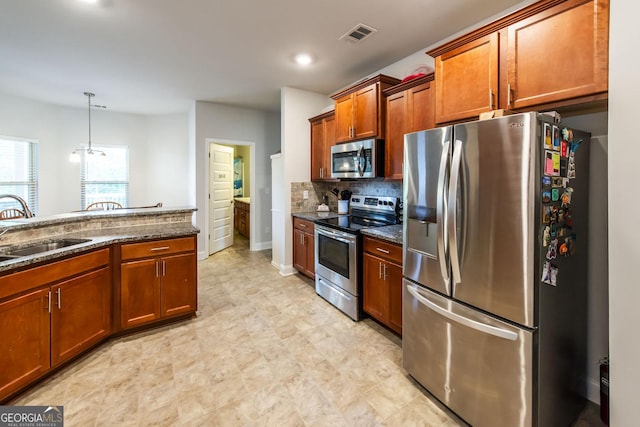 kitchen featuring appliances with stainless steel finishes, tasteful backsplash, dark stone counters, sink, and hanging light fixtures