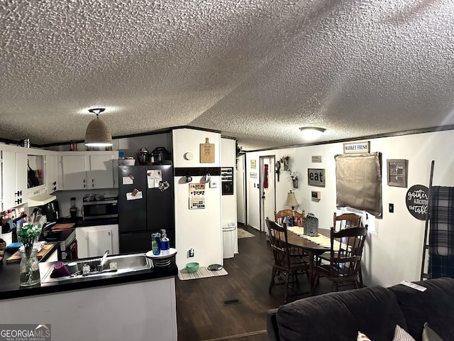 kitchen featuring black refrigerator, a textured ceiling, dark hardwood / wood-style flooring, sink, and white cabinetry