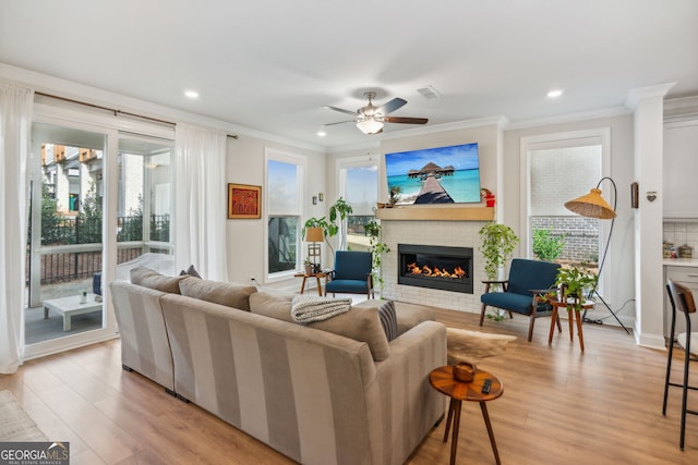 living room with ornamental molding, a brick fireplace, ceiling fan, and light wood-type flooring