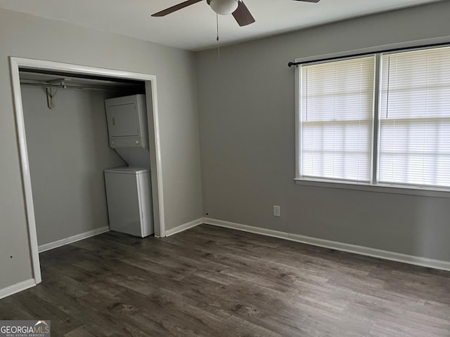 unfurnished bedroom featuring a closet, ceiling fan, stacked washer and dryer, and dark wood-type flooring