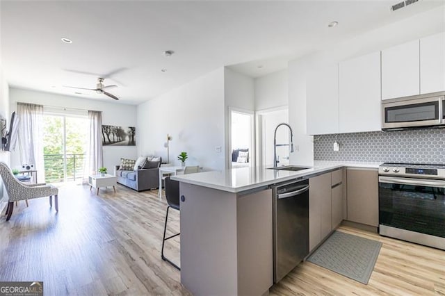 kitchen with kitchen peninsula, sink, appliances with stainless steel finishes, tasteful backsplash, and white cabinetry