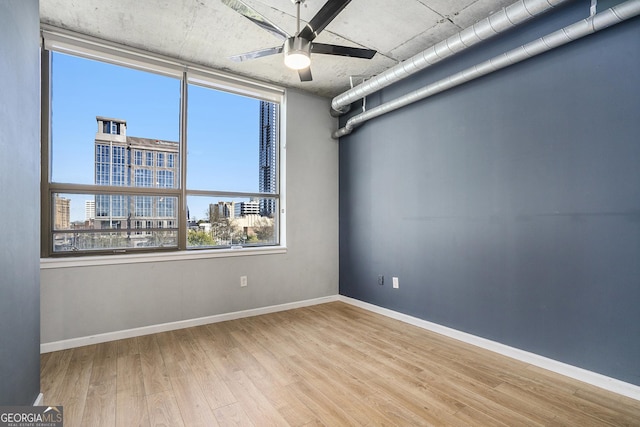 unfurnished room with a ceiling fan, baseboards, a city view, and light wood finished floors