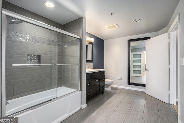 full bathroom with baseboards, combined bath / shower with glass door, vanity, and toilet