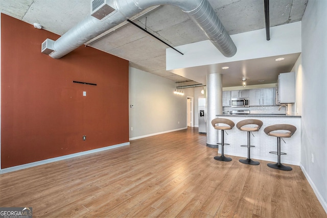 kitchen with kitchen peninsula, light wood-type flooring, appliances with stainless steel finishes, a kitchen breakfast bar, and white cabinets