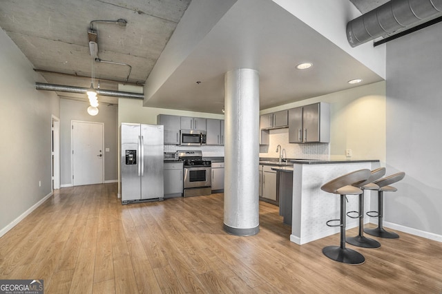 kitchen with light hardwood / wood-style floors, kitchen peninsula, appliances with stainless steel finishes, a kitchen breakfast bar, and gray cabinetry