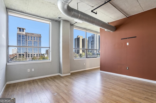 empty room with light wood-style floors, a view of city, and baseboards