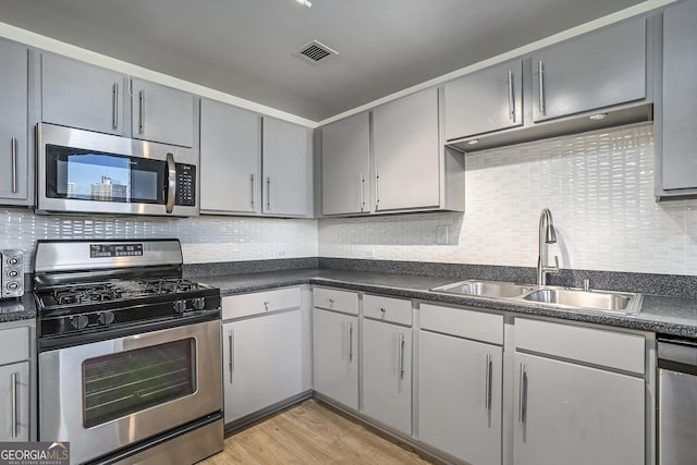 kitchen with stainless steel appliances, tasteful backsplash, sink, gray cabinets, and light wood-type flooring