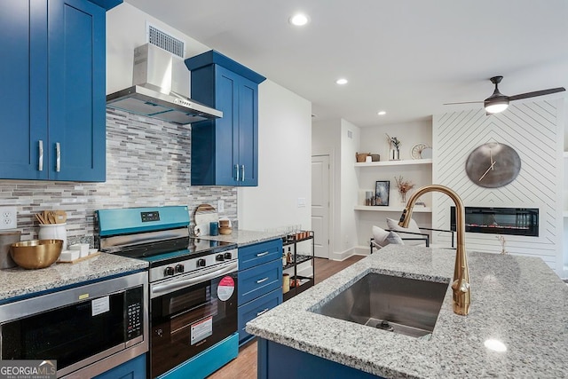 kitchen with blue cabinets, a sink, electric stove, wall chimney range hood, and built in microwave