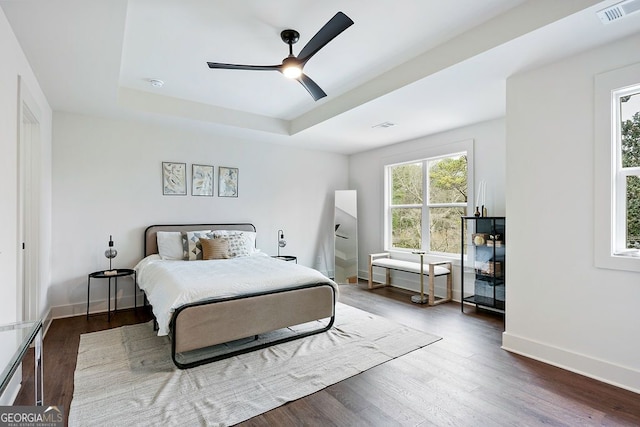 bedroom with wood finished floors, a raised ceiling, visible vents, and baseboards