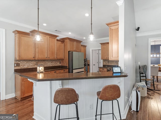 kitchen featuring a breakfast bar, stainless steel fridge, tasteful backsplash, decorative light fixtures, and kitchen peninsula