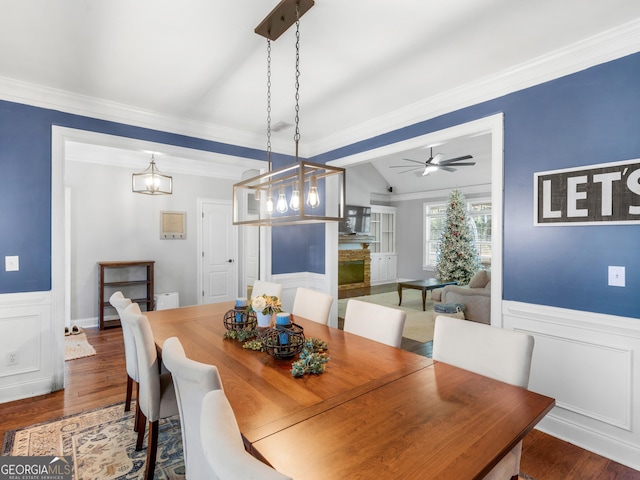 dining space with crown molding, ceiling fan with notable chandelier, dark wood-type flooring, and vaulted ceiling