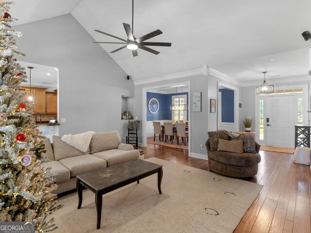 living room with ceiling fan with notable chandelier, hardwood / wood-style flooring, high vaulted ceiling, and a healthy amount of sunlight