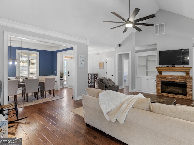 living room with built in shelves, ceiling fan with notable chandelier, dark wood-type flooring, a fireplace, and lofted ceiling