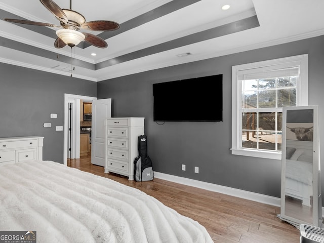 bedroom featuring a tray ceiling, ceiling fan, light wood-type flooring, and ornamental molding