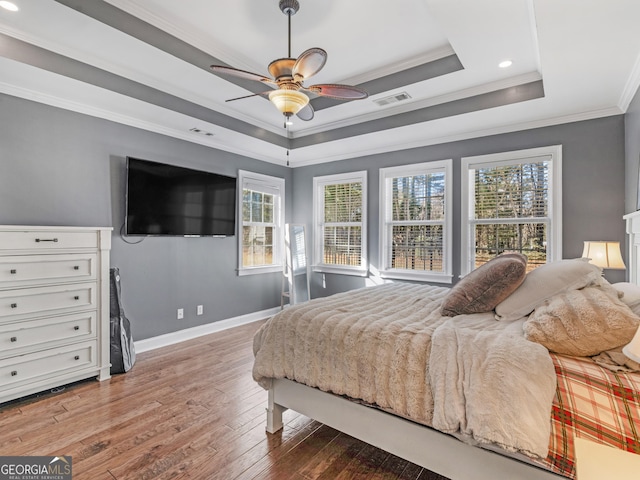 bedroom with hardwood / wood-style floors, ceiling fan, ornamental molding, and a tray ceiling