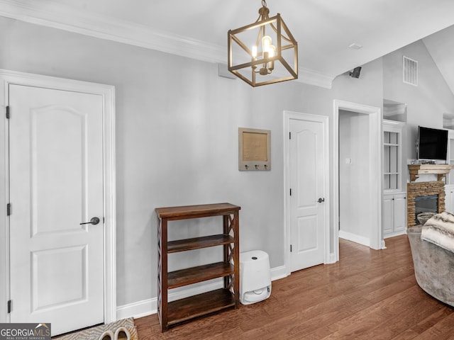 interior space with a fireplace, wood-type flooring, an inviting chandelier, and crown molding