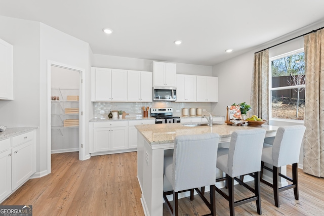 kitchen featuring sink, stainless steel appliances, white cabinetry, and an island with sink