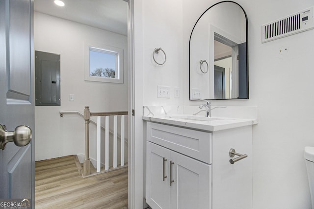 bathroom featuring hardwood / wood-style floors, vanity, electric panel, and toilet