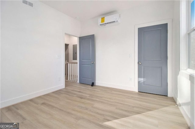 unfurnished bedroom featuring a wall mounted air conditioner, electric panel, and light hardwood / wood-style flooring