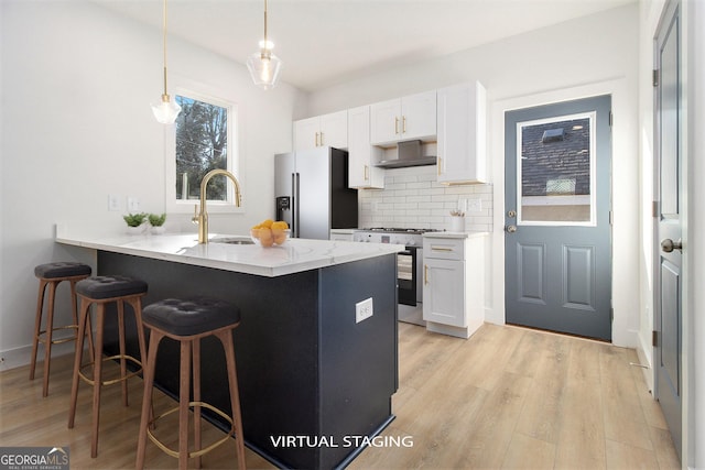 kitchen with decorative backsplash, appliances with stainless steel finishes, ventilation hood, white cabinets, and hanging light fixtures