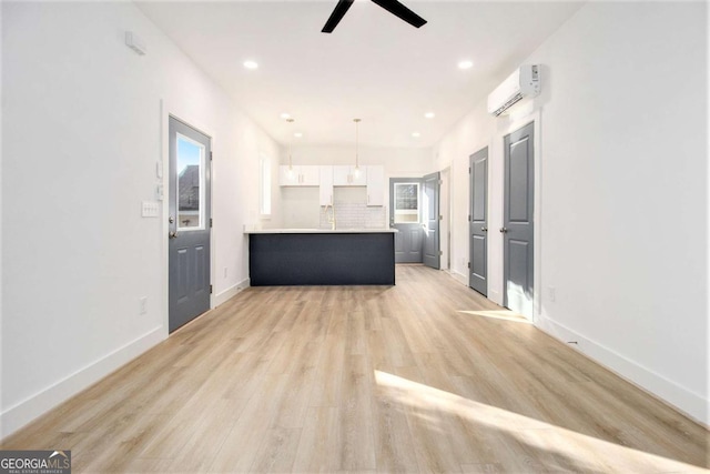 unfurnished living room featuring a wall mounted air conditioner, light wood-type flooring, and ceiling fan