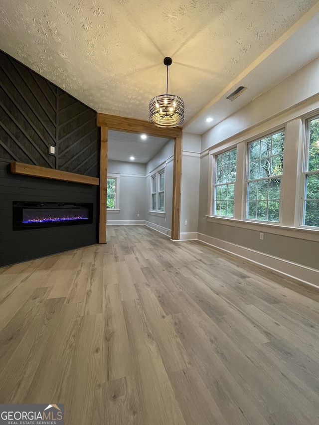 unfurnished living room featuring a healthy amount of sunlight, a chandelier, wood-type flooring, a textured ceiling, and a fireplace