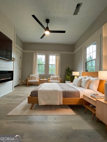 bedroom featuring multiple windows, a large fireplace, light hardwood / wood-style flooring, and ceiling fan