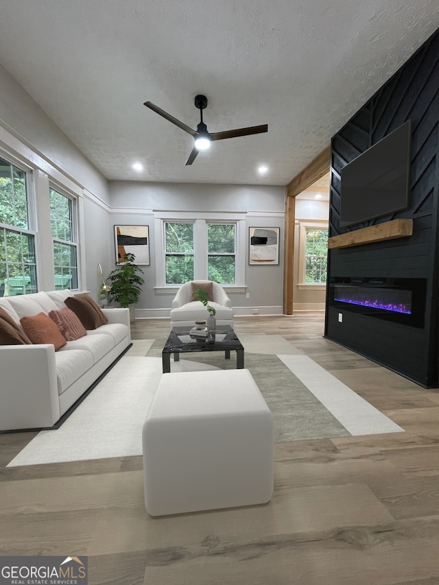 living room with a fireplace, light hardwood / wood-style flooring, ceiling fan, and plenty of natural light