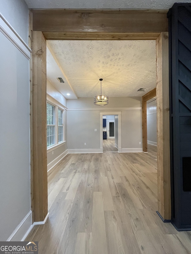 unfurnished living room with light hardwood / wood-style flooring, a textured ceiling, and a notable chandelier