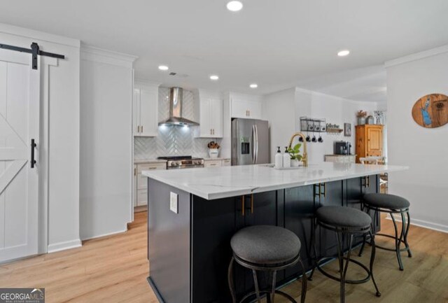 kitchen featuring stainless steel fridge, wall chimney exhaust hood, a barn door, white cabinets, and a large island