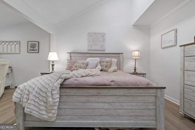 bedroom featuring light wood-type flooring, vaulted ceiling, and ornamental molding