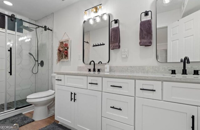 bathroom featuring hardwood / wood-style floors, vanity, a shower with shower door, and toilet