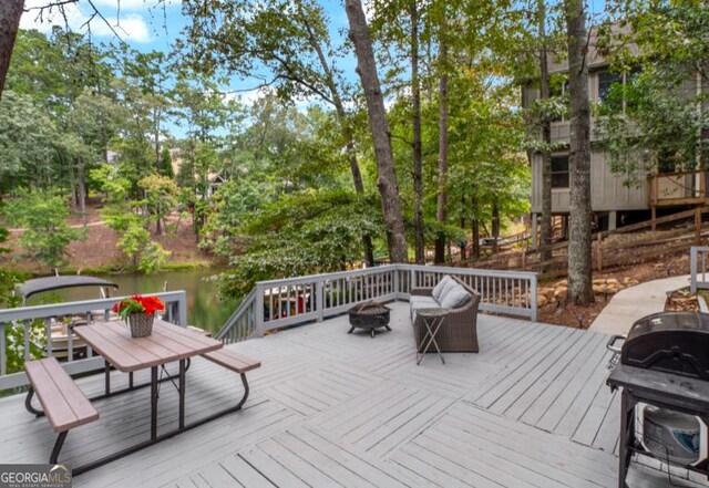 deck featuring area for grilling, a water view, and an outdoor fire pit