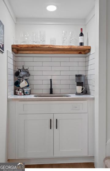 bar featuring white cabinets, decorative backsplash, and sink