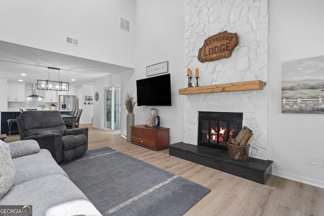 living room featuring a chandelier, wood-type flooring, a stone fireplace, and a high ceiling