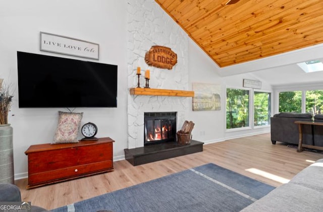 living room with a skylight, wooden ceiling, a stone fireplace, high vaulted ceiling, and hardwood / wood-style floors