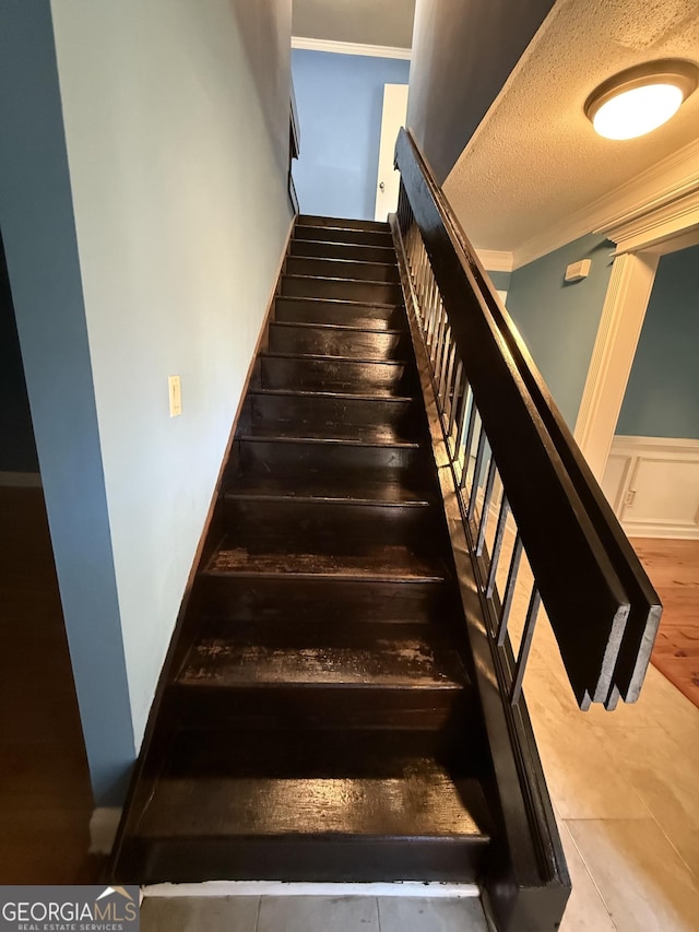 stairway with a textured ceiling and ornamental molding