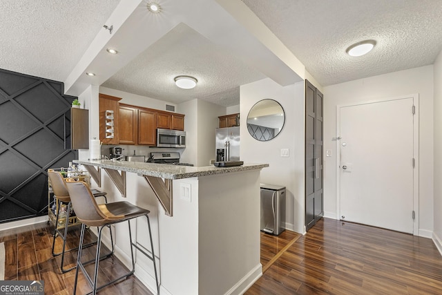 kitchen with a textured ceiling, appliances with stainless steel finishes, dark hardwood / wood-style flooring, kitchen peninsula, and a breakfast bar area