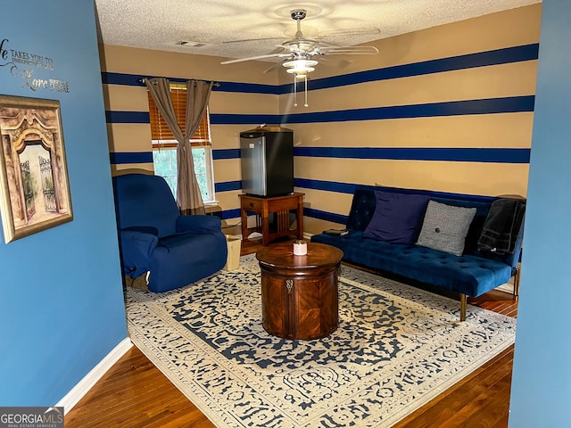 living area featuring ceiling fan, wood-type flooring, and a textured ceiling