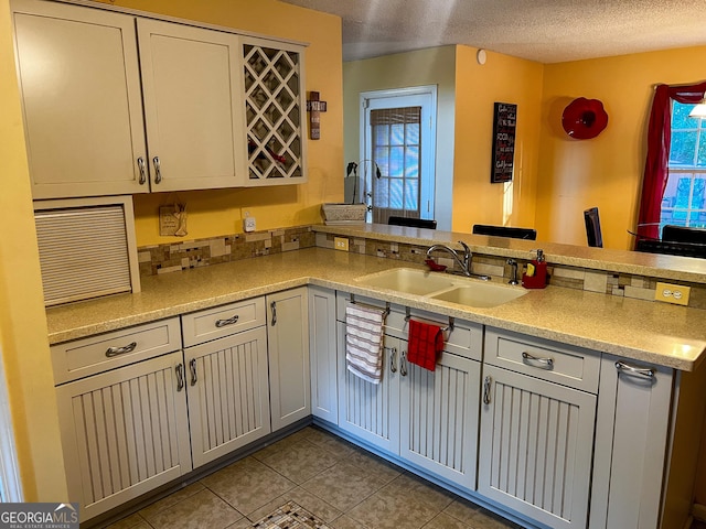 kitchen featuring kitchen peninsula, a textured ceiling, light tile patterned flooring, and sink