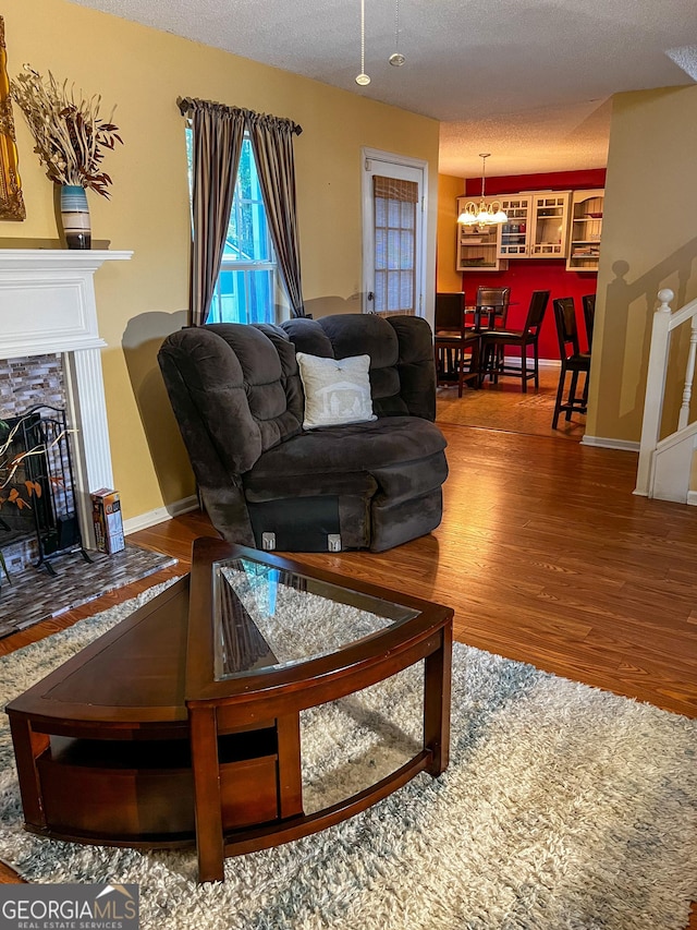 living room with hardwood / wood-style floors, a textured ceiling, an inviting chandelier, and a stone fireplace