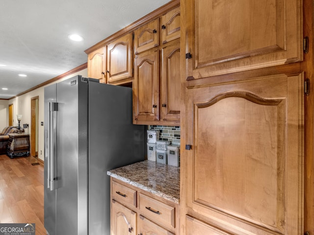 kitchen featuring light stone counters, backsplash, light hardwood / wood-style floors, high end fridge, and ornamental molding