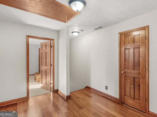 unfurnished room with a textured ceiling and light wood-type flooring