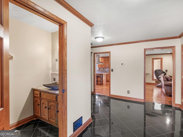 hallway with dark tile patterned flooring, a textured ceiling, and ornamental molding