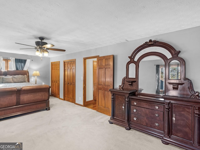 bedroom with multiple closets, ceiling fan, light carpet, and a textured ceiling