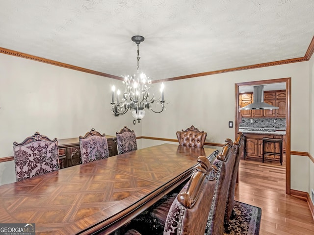 dining space featuring an inviting chandelier, ornamental molding, a textured ceiling, and light hardwood / wood-style flooring